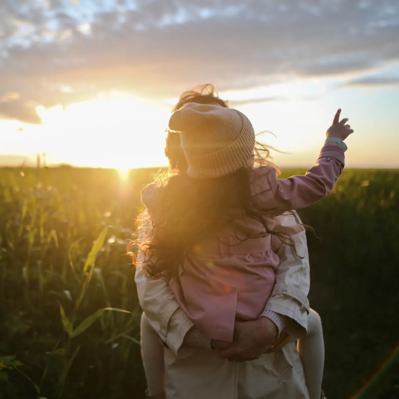 Mother holding daughter in field at sunset