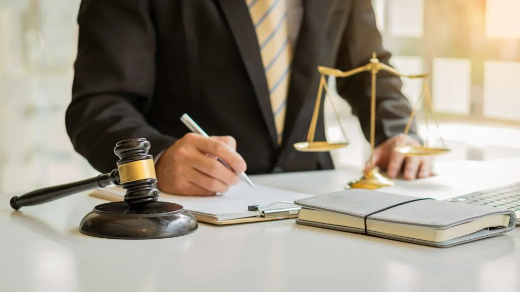 Divorce lawyer mediating between couple during legal consultation with gavel, wedding rings, and justice scale on desk.
