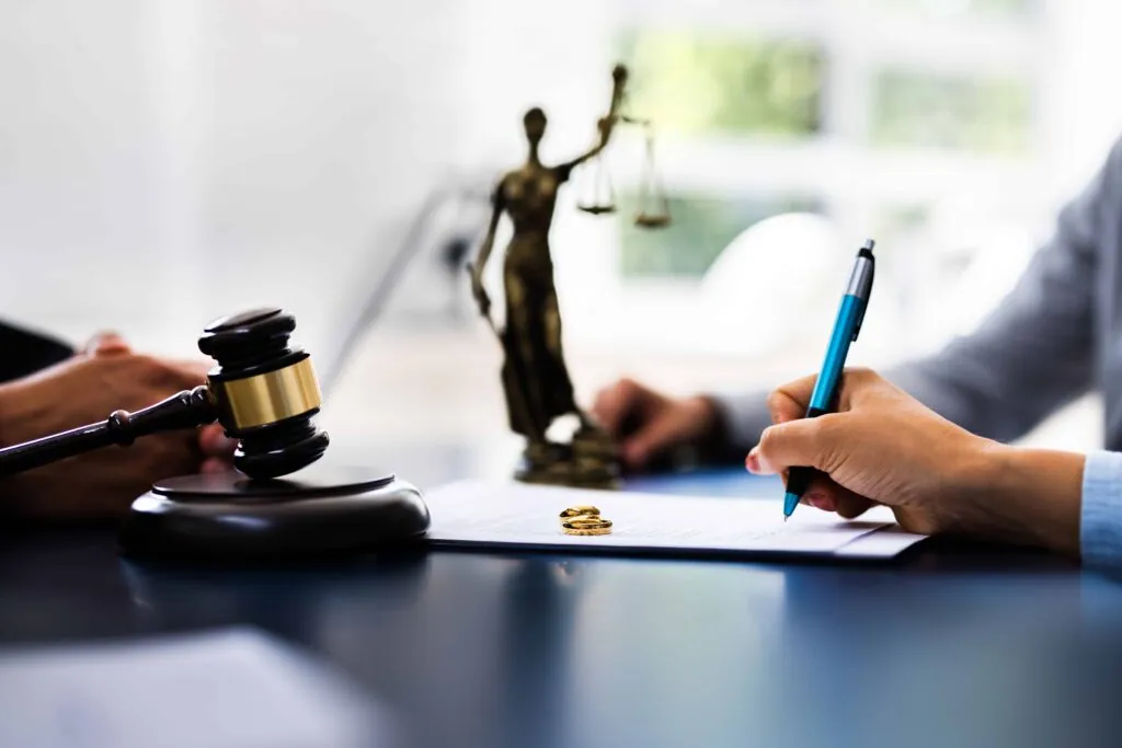 Divorce lawyer reviewing legal documents with client, gavel and wedding rings on desk symbolizing marriage dissolution. Divorce lawyer reviewing legal documents with client, gavel and wedding rings on desk symbolizing marriage dissolution.