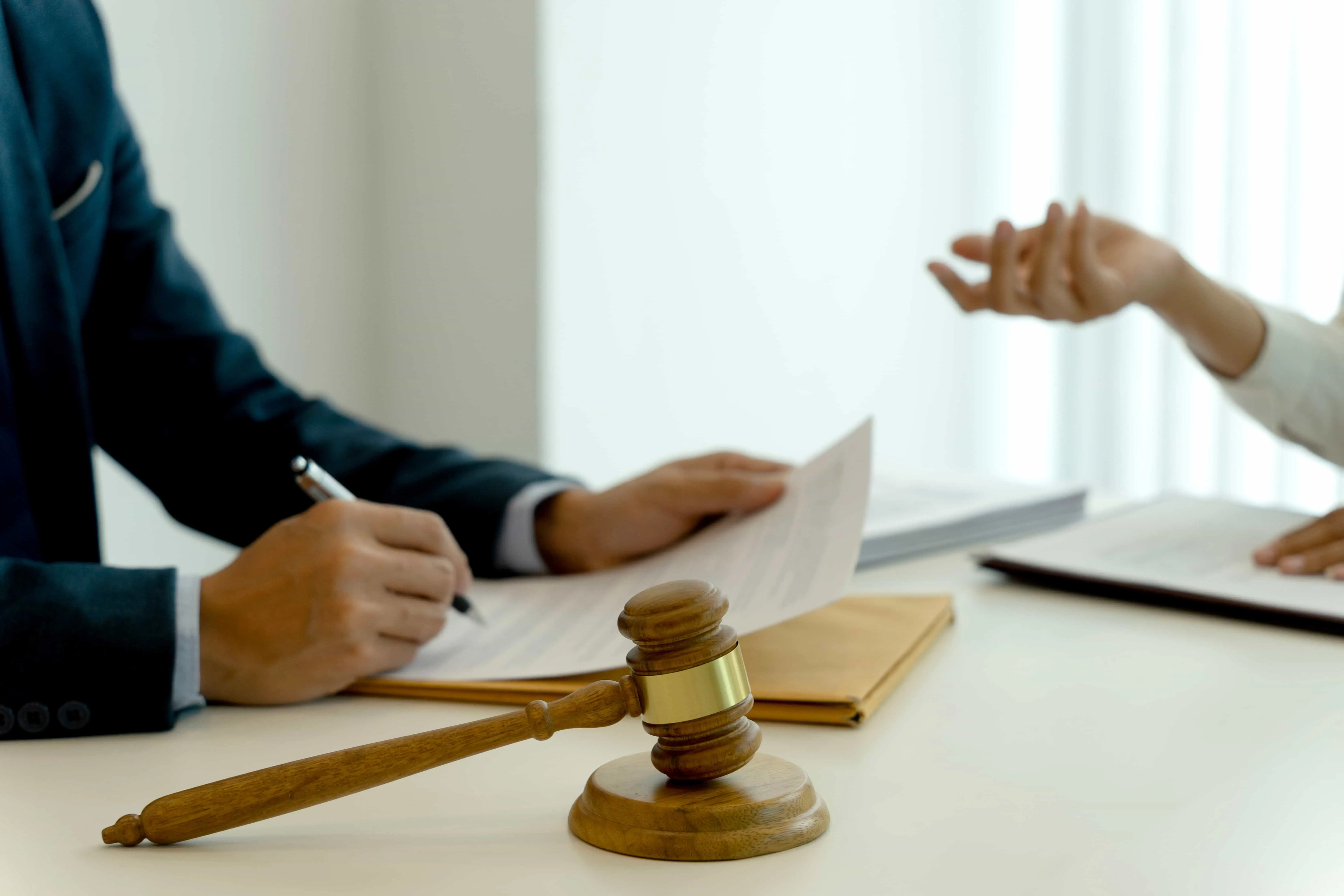 Lawyer reviewing legal documents with client at desk, gavel symbolizing justice and legal consultation.