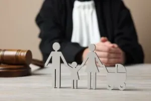 Family law. Judge with gavel sitting at white wooden table, focus on figure of parents and children