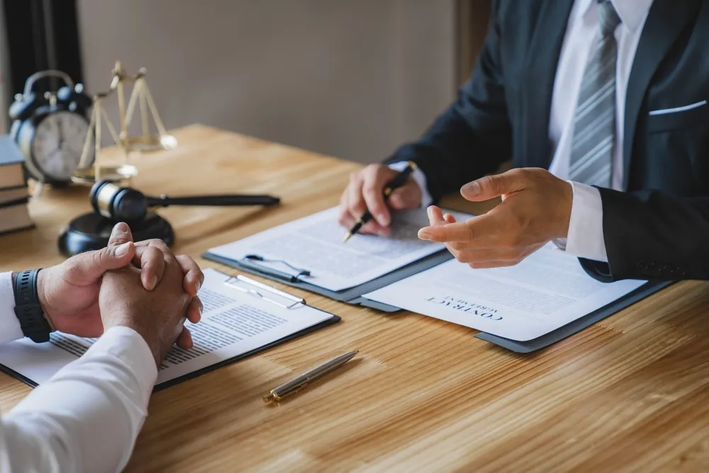 Business lawyer consulting with a client, reviewing contract documents and discussing legal matters in an office or courtroom setting