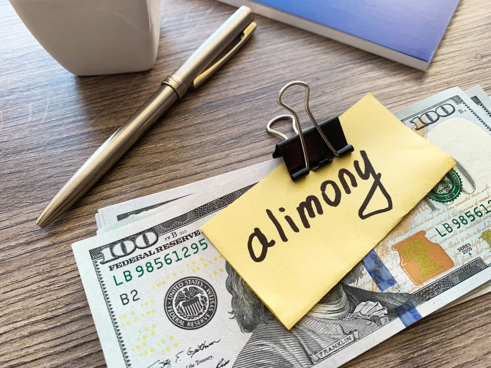 Stack of dollar bills with an alimony sign, symbolizing divorce, separation, and spousal support payments.