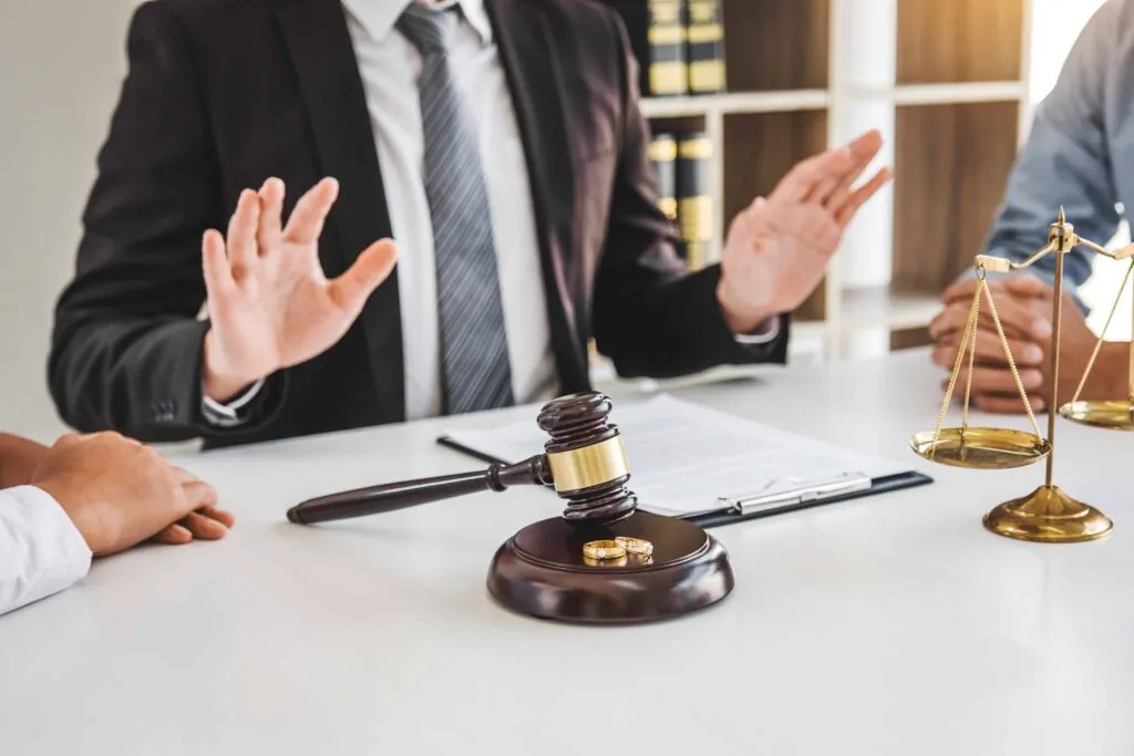 Divorce lawyer mediating between couple during legal consultation with gavel, wedding rings, and justice scale on desk. Divorce lawyer mediating between couple during legal consultation with gavel, wedding rings, and justice scale on desk.