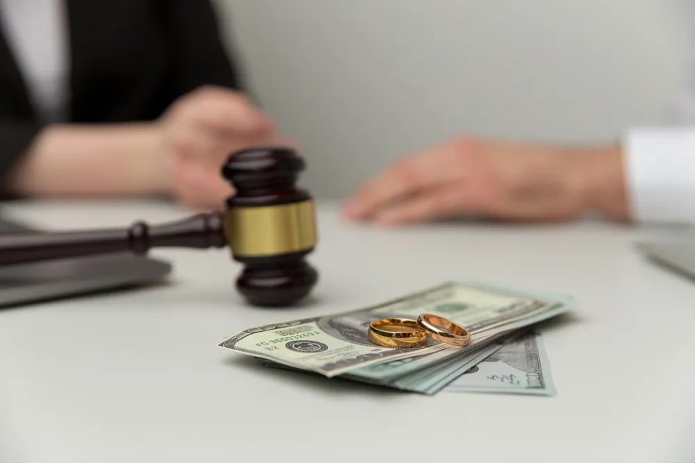 Gavel, cash, and wedding rings on a table during a legal discussion.