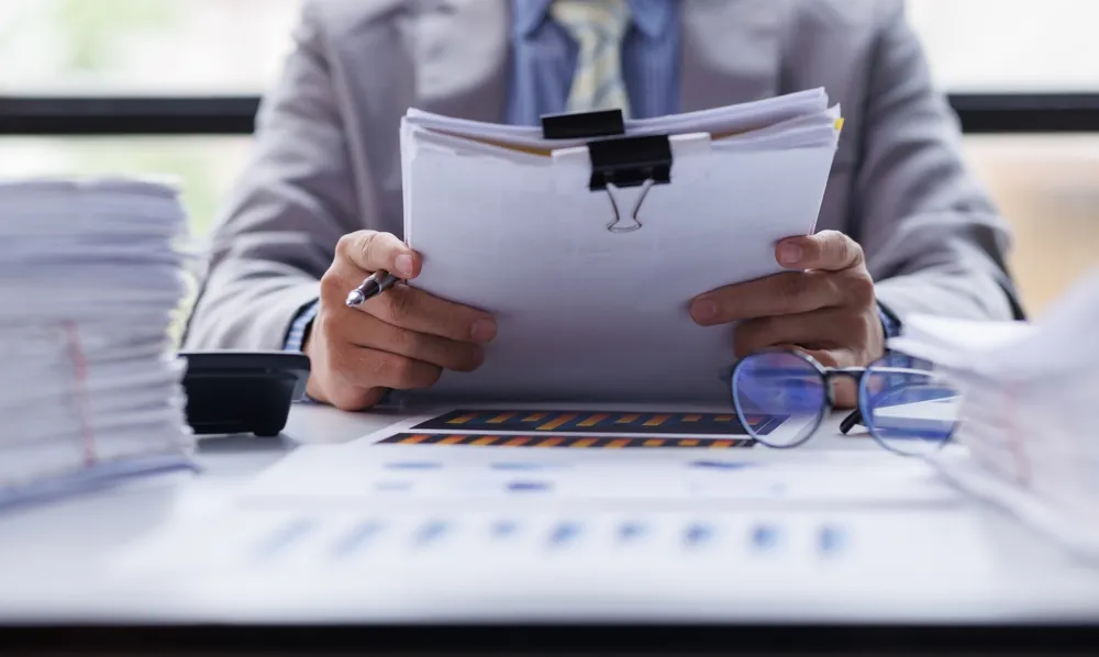 Businessperson reviewing stacks of documents at a desk.